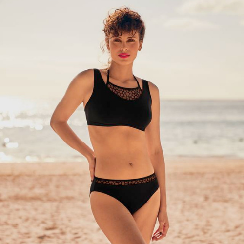 Mulher na praia com biquíni preto, com pormenores rendados no decote e na cintura