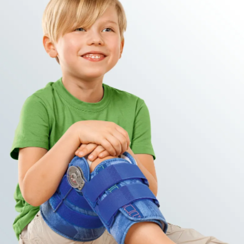 Menino sentado com a joelheira azul articulada colocada, presa por três tiras de velcro