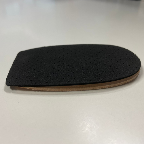 Talonete com cobertura preta microperfurada sobre base bege, visto de lado numa mesa branca